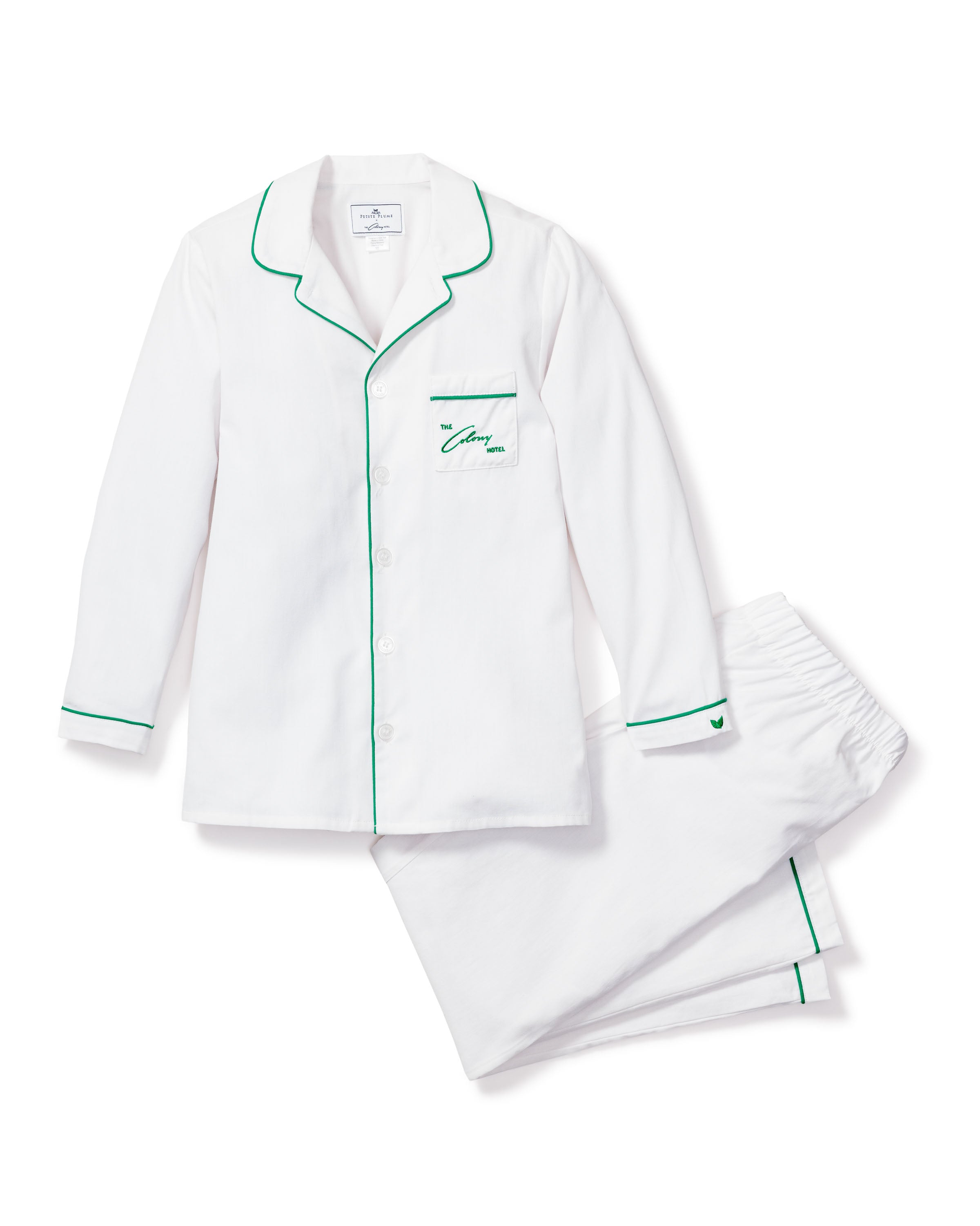 Experience luxury with the Petite Plumes Colony Hotel x Petite Plume Kids Pajama Set in white with green piping. This set includes a long-sleeve button-up top featuring a collar, left chest pocket embossed with The Harmony, and pants, all reminiscent of the Colony Hotel elegance.