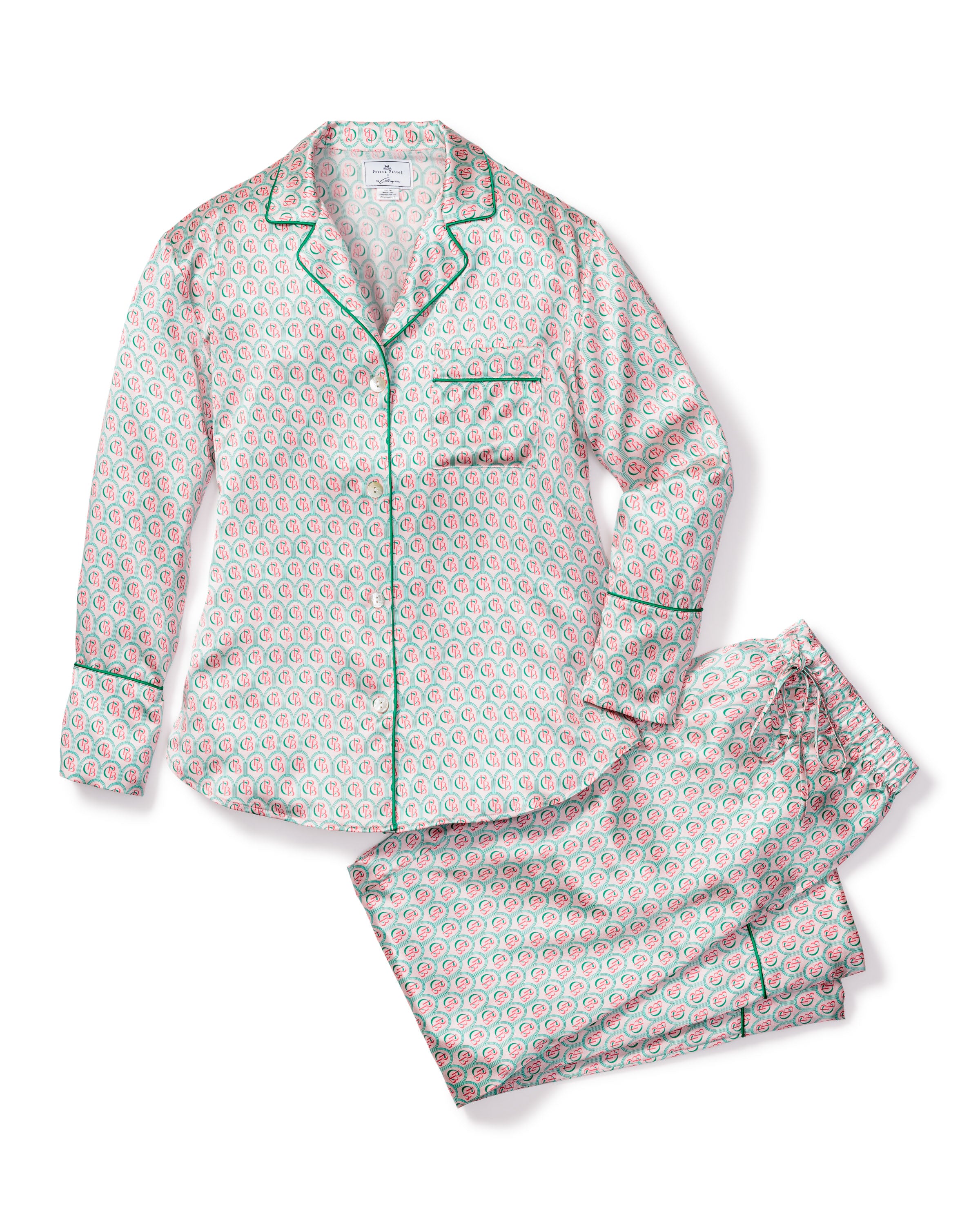 Indulge in the luxury of the Colony Hotel x Petite Plume Womens Silk Pajama Set, featuring a white base with red and green floral patterns. The long-sleeved top has a collar, buttons, and green piping, while the pants provide a relaxed fit for ultimate comfort.