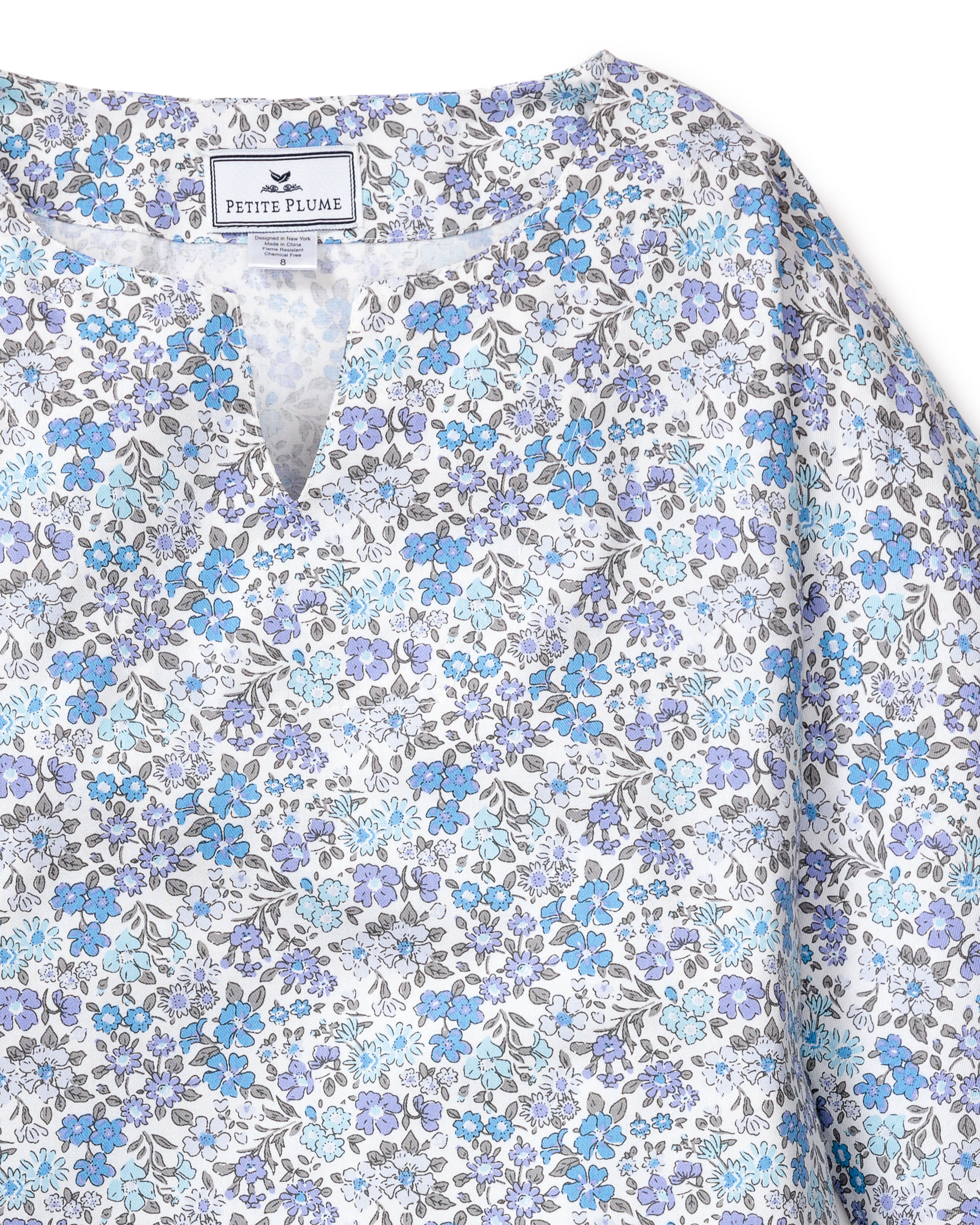 The Girls Twill Caftan in Fleur DAzur by Petite Plume is a blue and grey floral-patterned sleepwear piece with a V-neck, crafted from breathable cotton. Delicate flowers adorn the white background, creating a vintage-inspired print.