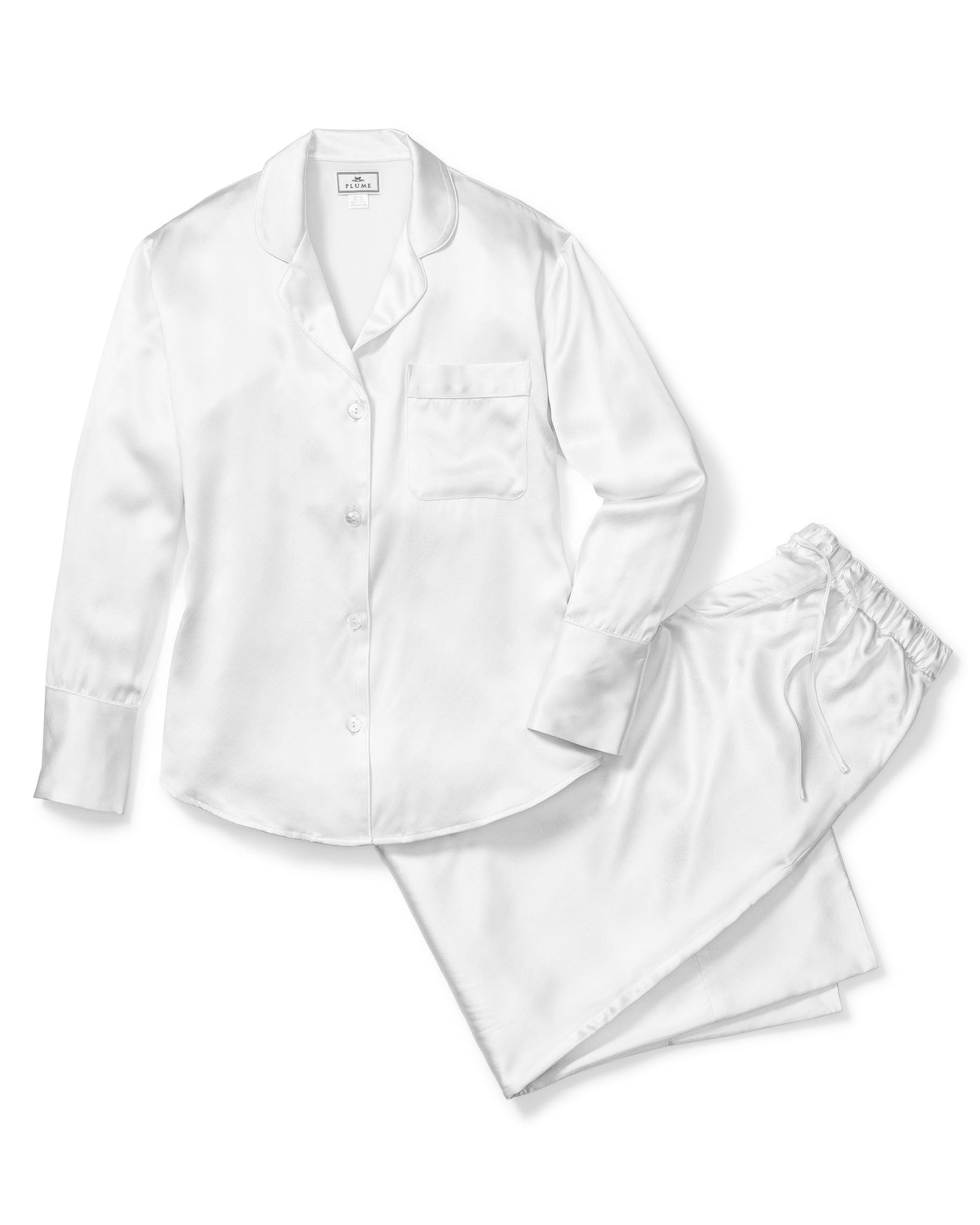 The Womens Silk Pajama Set in White by Petite Plume includes luxury sleepwear with a long-sleeve button-up shirt and chest pocket, paired with matching pants featuring an elastic waistband. The 22mm silk fabric is smooth and shiny.
