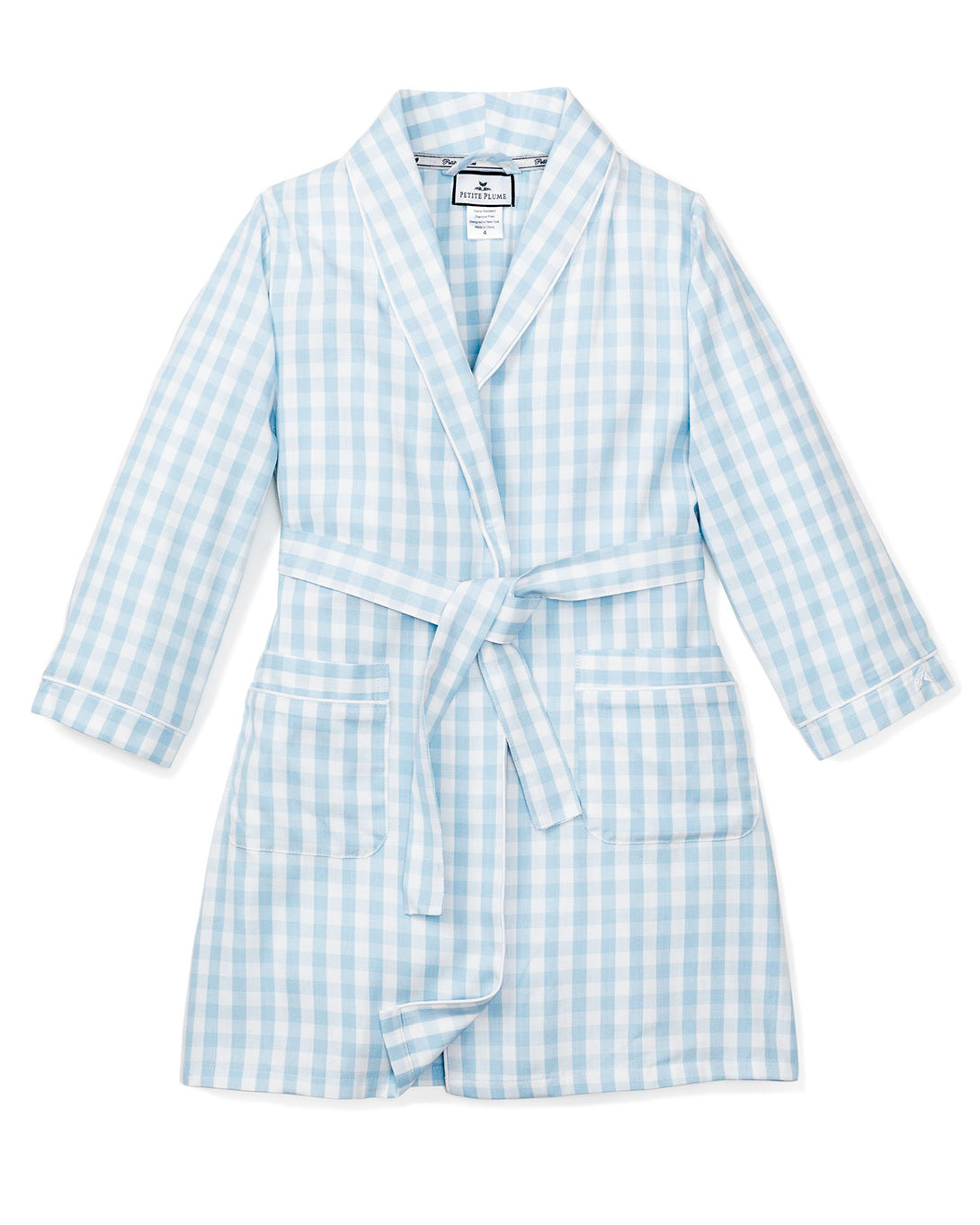 The Kids Twill Robe by Petite Plume features a light blue gingham print with long sleeves, a waist tie, two front pockets, and a shawl collar. Its displayed on a white background and crafted from chemical-free materials for comfort and safety.