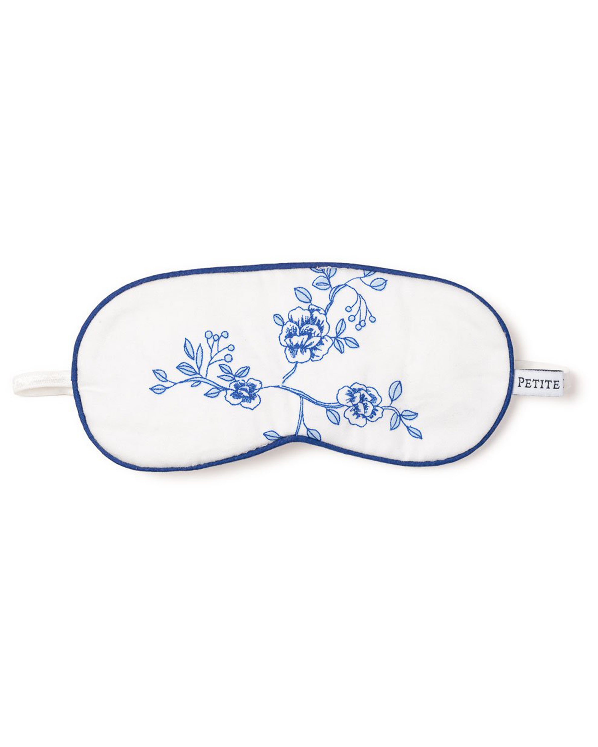 The Kids Sleep Mask in Indigo Floral by Petite Plume features blue floral embroidery with blossoms and leaves, trimmed in blue with an elastic strap. Its small tag reads PETITE PLUME, making it a dreamy, customizable gift.