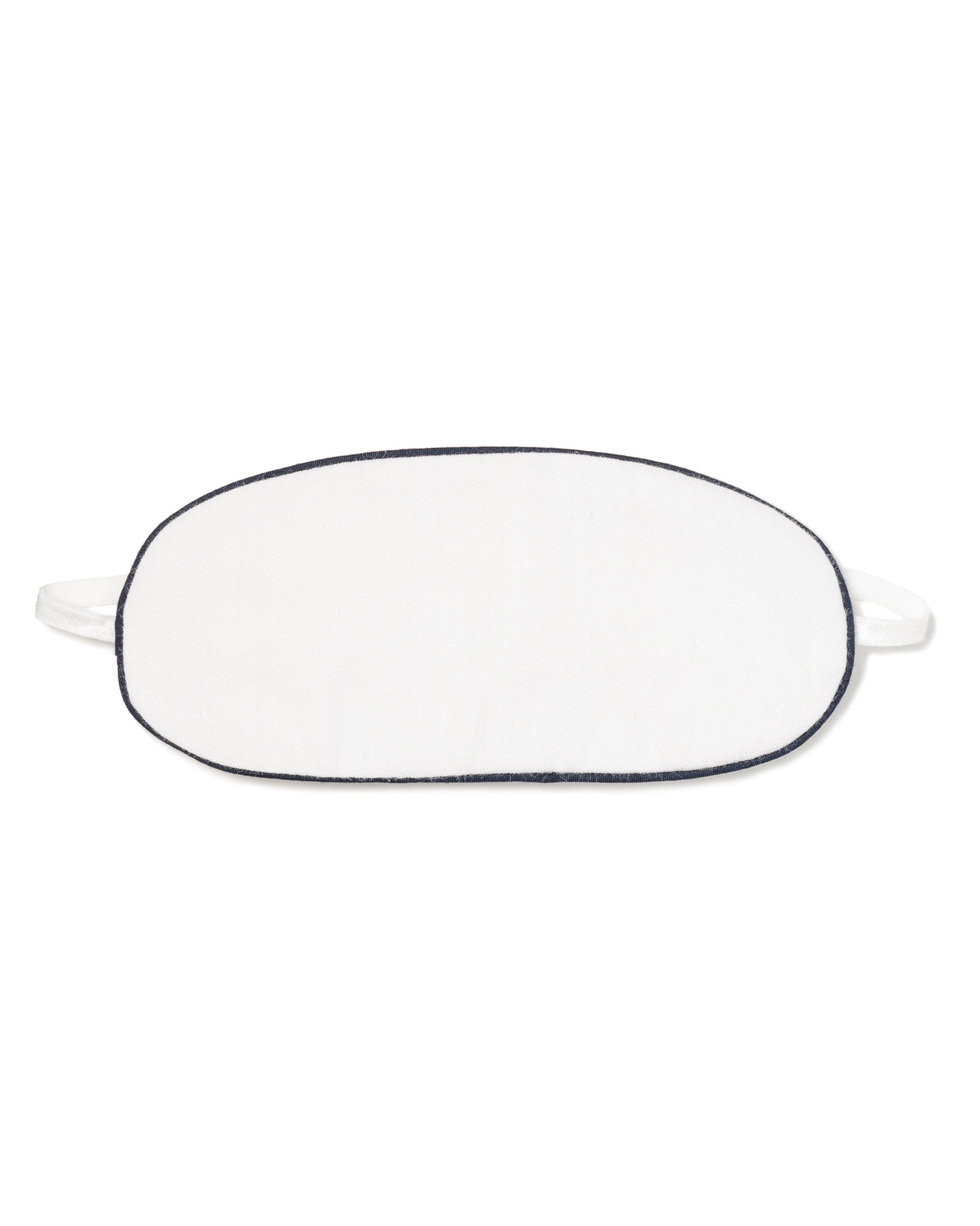 The Kids Twill Sleep Mask in White with Navy Piping by Petite Plume offers a touch of luxurious sleepwear. This oval-shaped mask is perfect for restful nights and pairs elegantly with other bedtime accessories, set gracefully against a white background.