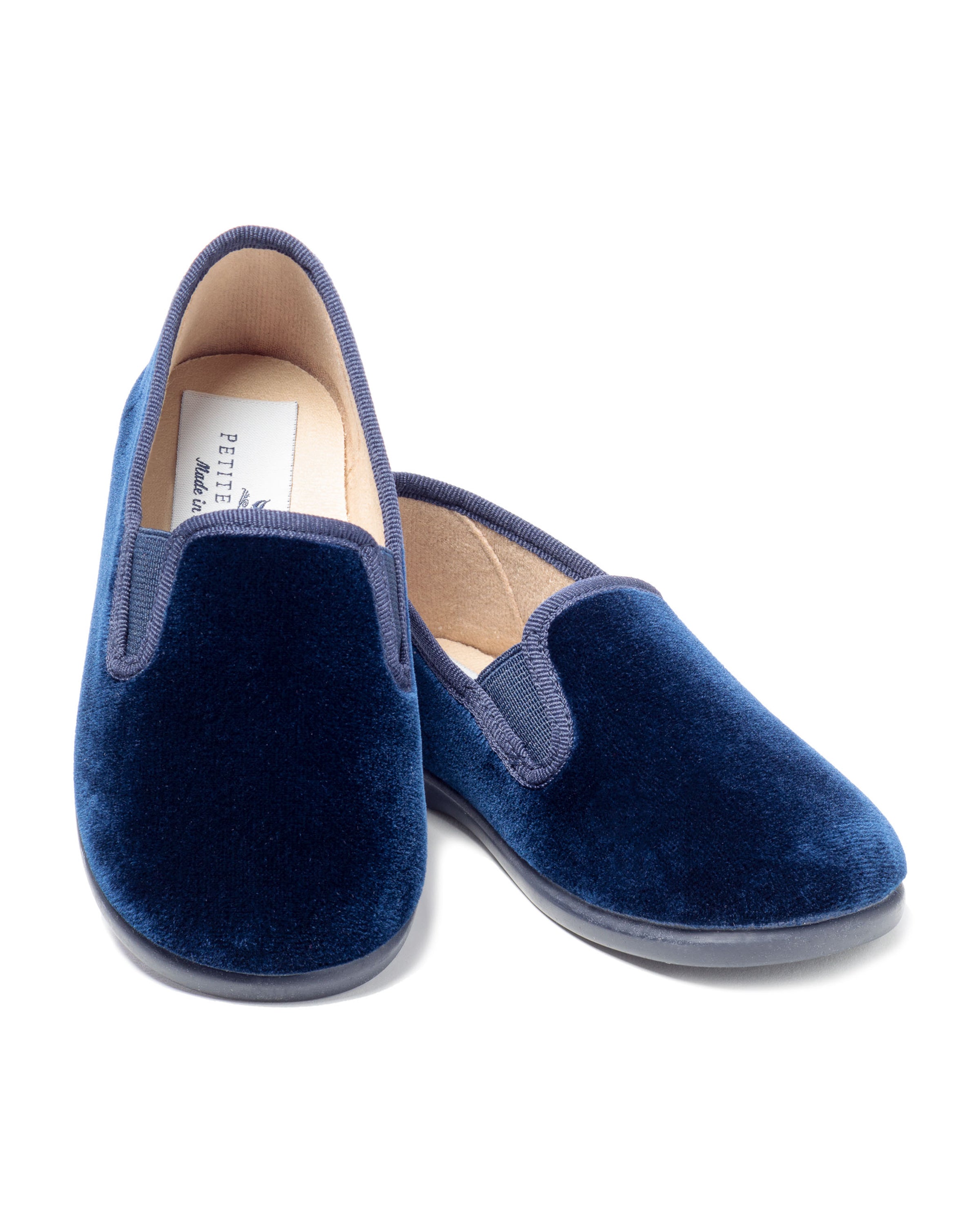 The Kids Gable Slipper by Petite Plume in navy velvet features a tan interior and black soles, showcasing the elegance of luxury slippers, set against a white background.