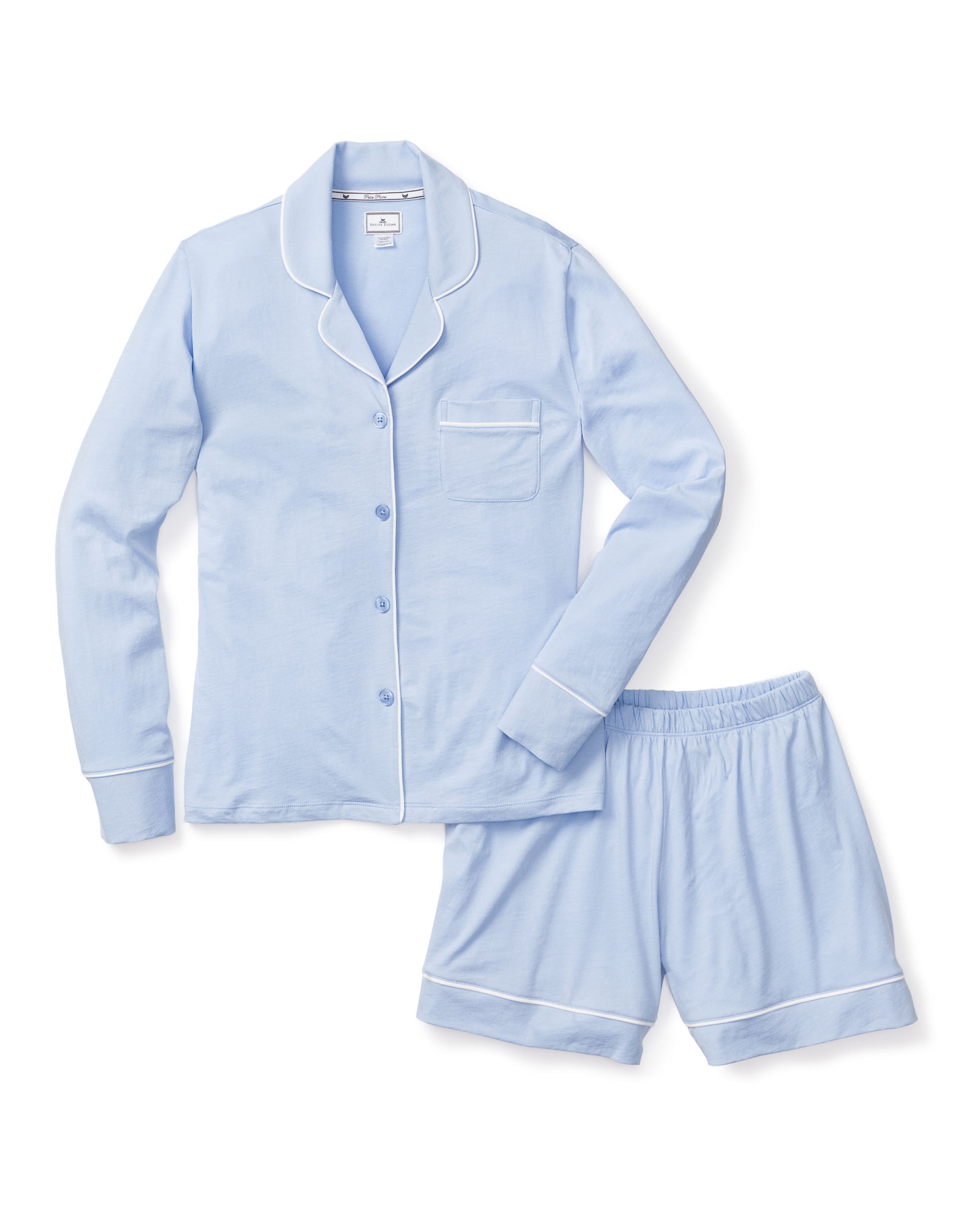 The Petite Plume Womens Pima Pajama Short Set in Periwinkle features a long-sleeve button-up top with a chest pocket and white piping, paired with matching shorts accented by white piping along the hem. Made from luxurious Peruvian Pima cotton, these classic PJs ensure comfort and style.