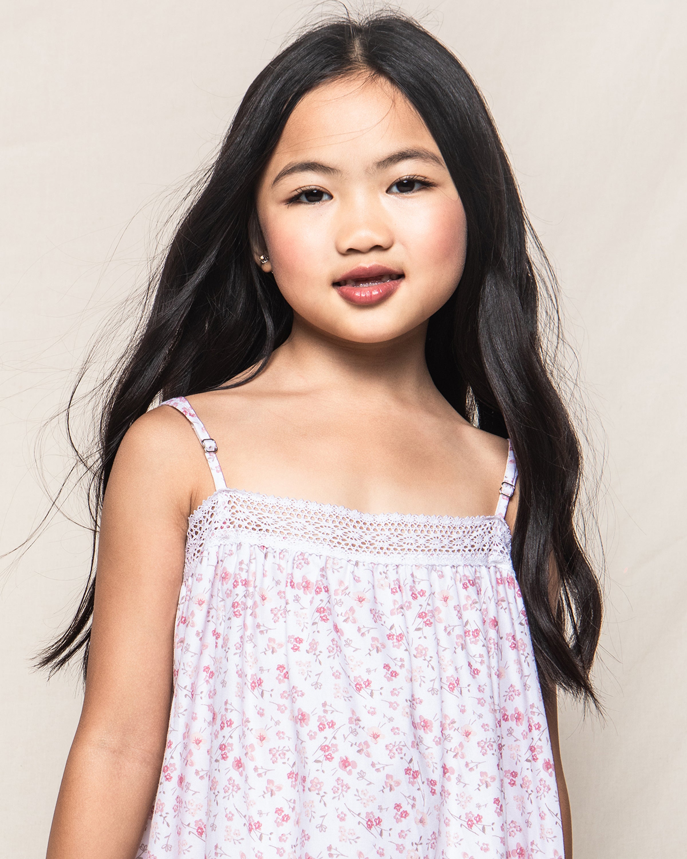 A young girl with long dark hair wears Petite Plumes Girls Twill Lily Nightgown in Dorset Floral. She stands against a neutral background, looking confidently at the camera with a slight smile, embodying luxury sleepwear.