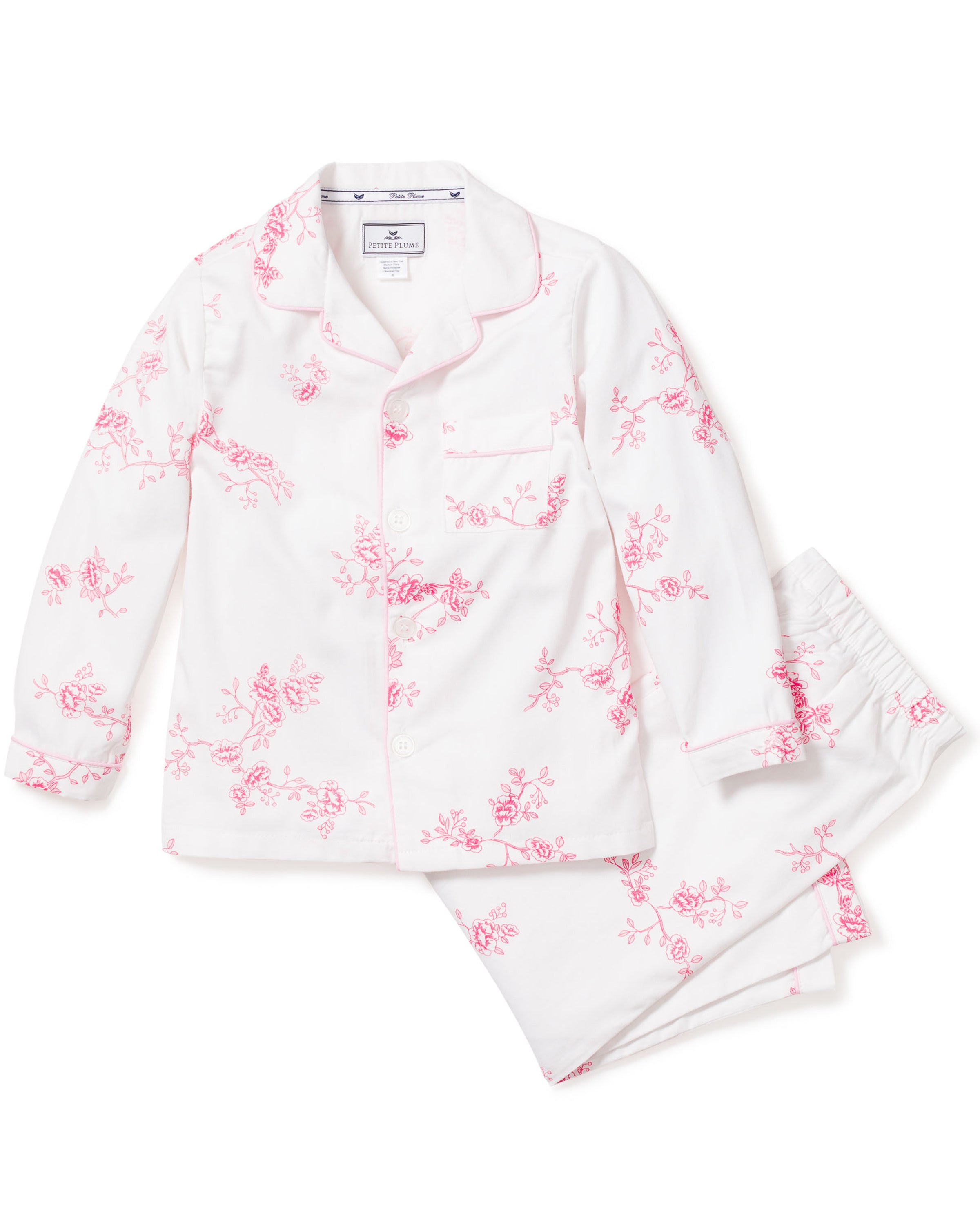 The Kids Twill Pajama Set in English Rose Floral by Petite Plume features a white, long-sleeved top with pink vintage floral prints, a collar, buttons, and chest pocket. The pants provide comfort with an elastic waistband, epitomizing luxurious sleepwear.