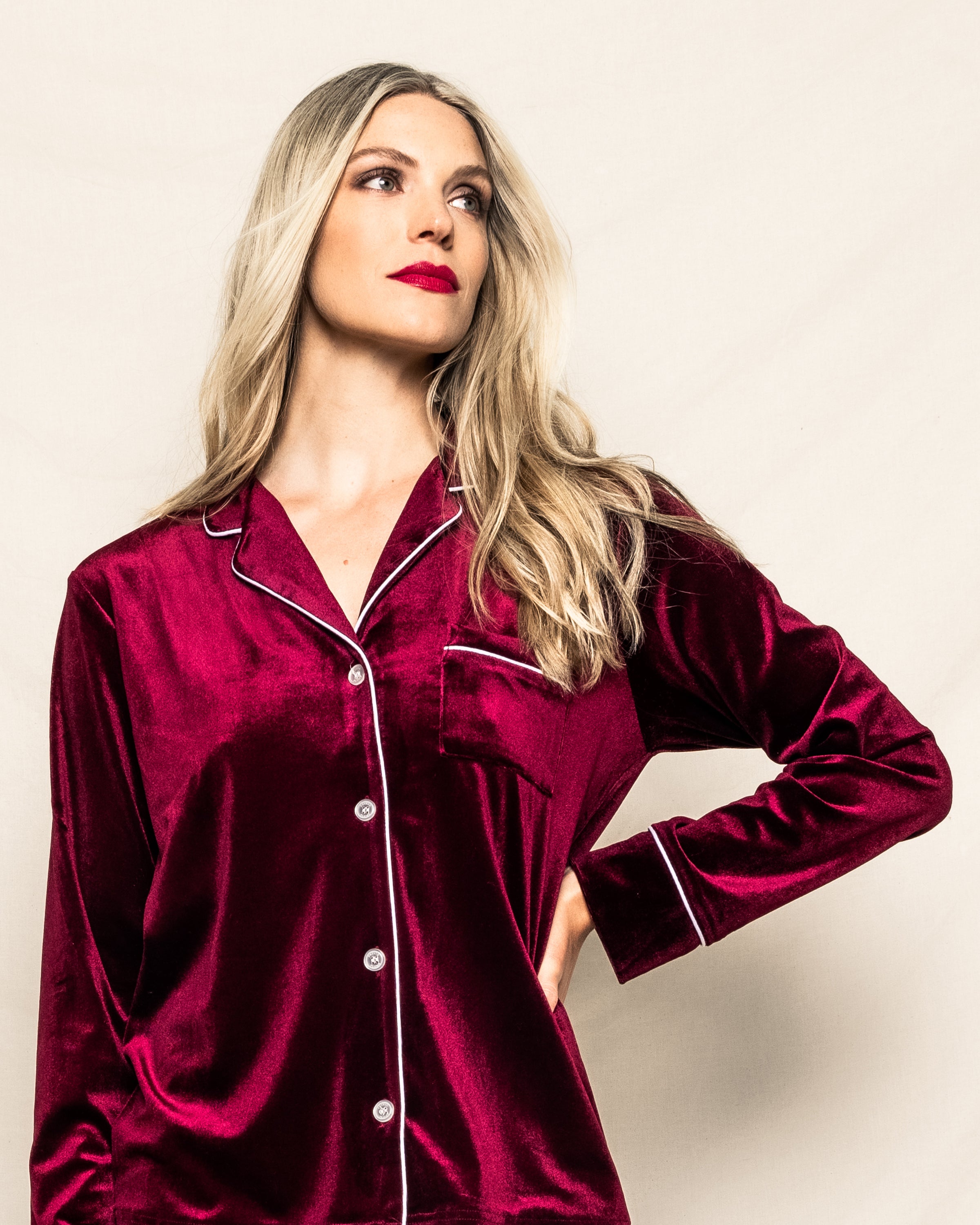 A person with long blonde hair models the Womens Velour Pajama Set in Royal Garnet by Petite Plume. They pose against a neutral background, exuding a confident expression that evokes classic Hollywood elegance.