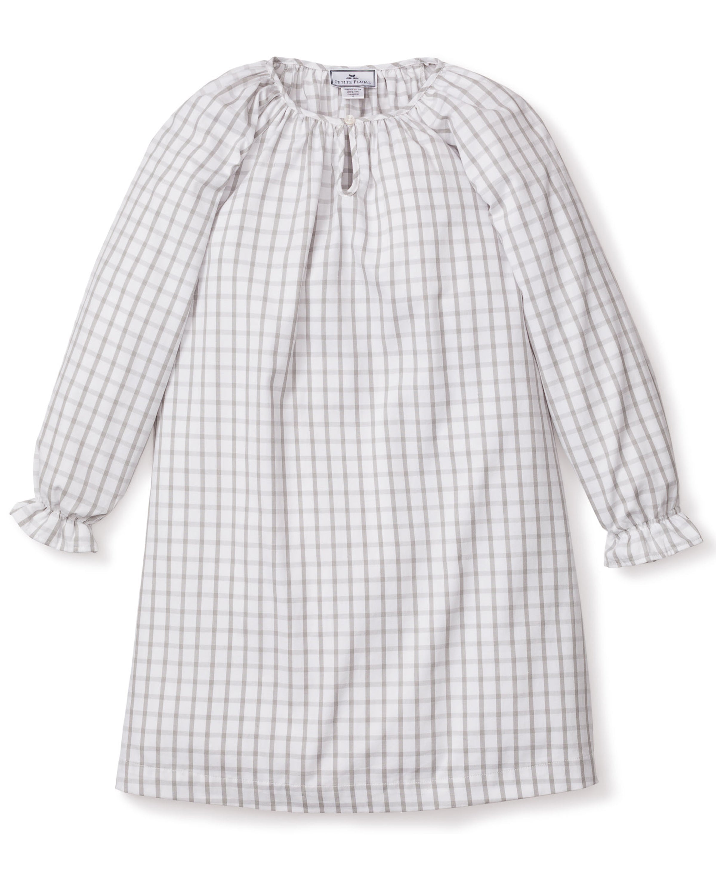 The Girls Twill Delphine Nightgown in Regent Tattersall by Petite Plume is a knee-length, long-sleeved dress with a gray and white checkered pattern. Made from yarn-dyed cotton, it has a round neckline with a keyhole opening and ruffled cuffs. The soft, lightweight fabric is ideal for casual wear.
