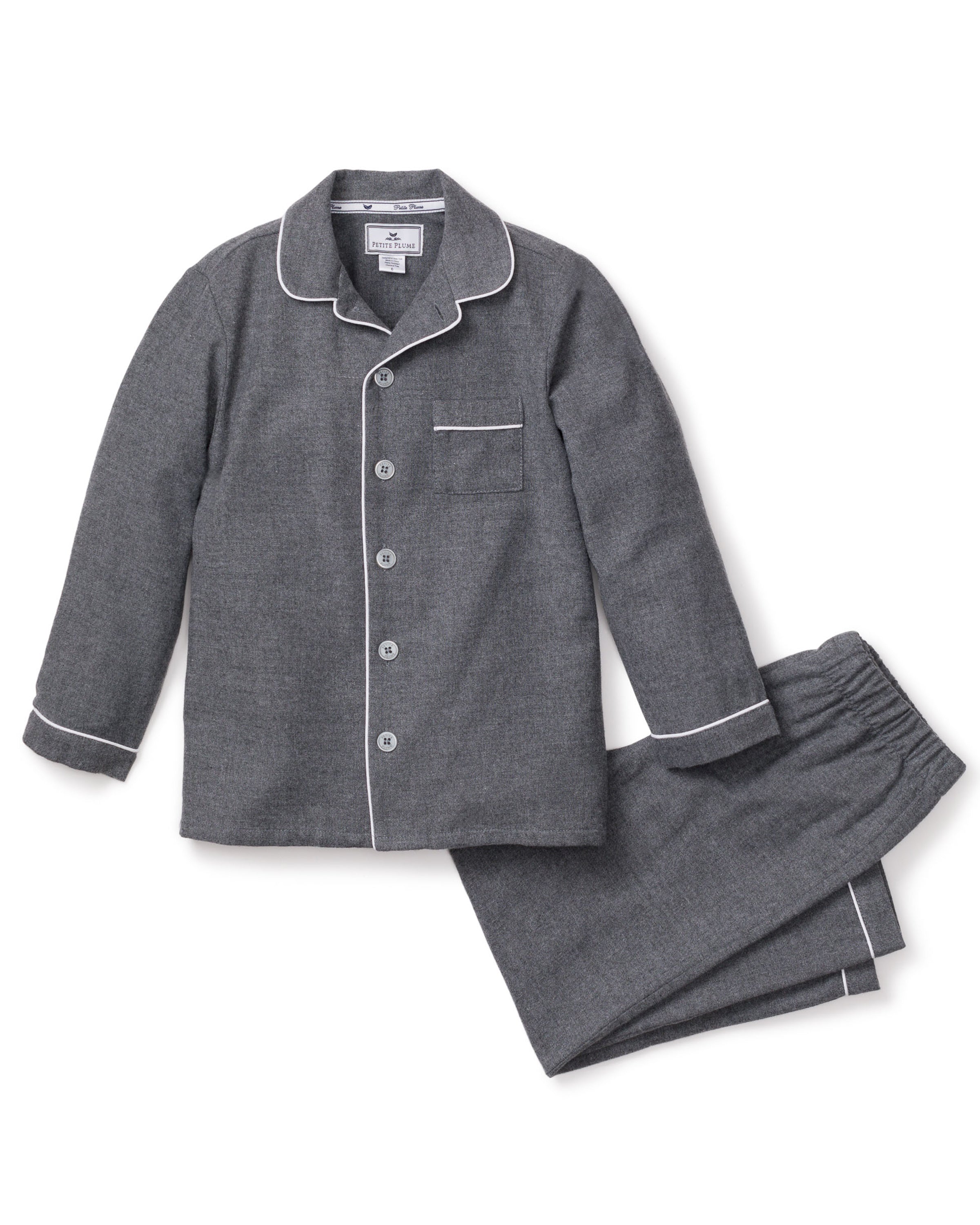 The Kids Flannel Pajama Set in Grey by Petite Plume offers a cozy design with white piping, featuring a button-up top with a chest pocket and pants with an elastic waistband. Made from soft, flame-retardant fabric, it ensures both comfort and safety.