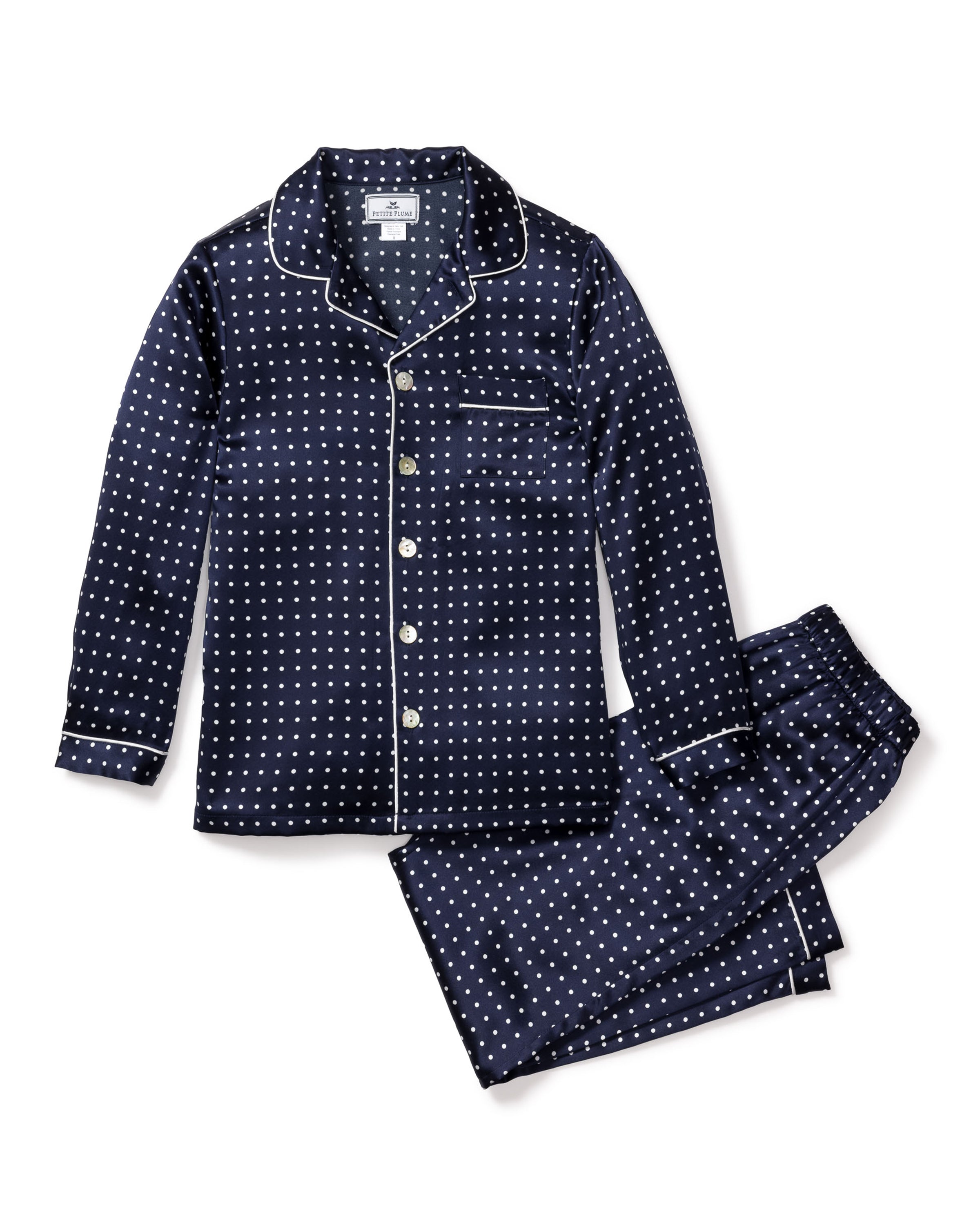 The Kids Silk Pajama Set in Navy Polka Dot by Petite Plume features a luxurious long-sleeve button-up shirt with white piping, a chest pocket, and matching pants for a stylish night’s rest.